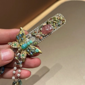 Detail of vintage butterfly hair clip with green crystals and long beaded tassels