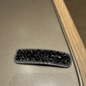 Detailansicht einer rechteckigen Haarspange mit schwarzen Steinen und hellen Kristallen