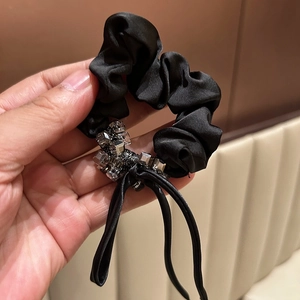 Elegant black satin scrunchie with faceted beads and long tassels held by hand