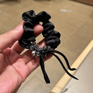 Detail of elegant black satin scrunchie with crystal clusters and delicate ribbons
