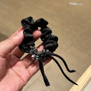 Detail of elegant black satin scrunchie featuring sparkling rhinestones and long streamers