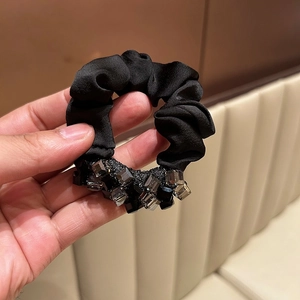 Close-up of black satin scrunchie with faceted crystal accents and pleated fabric texture