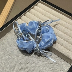 Detail eines hellblauen Haargummis mit Kristallperlen auf einem beigen Samttablett