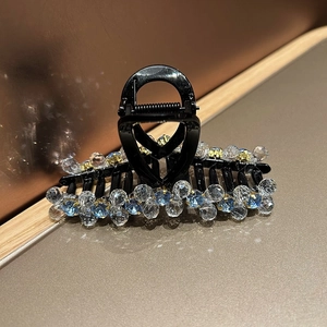 Close-up of elegant black hair claw clip with faceted blue and clear crystal beads