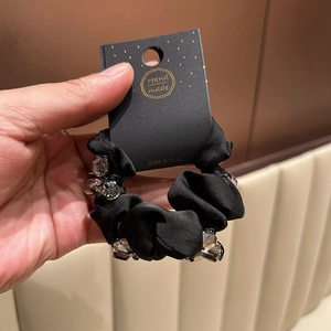 Detailed macro view of black satin scrunchie featuring faceted crystals and handmade tag