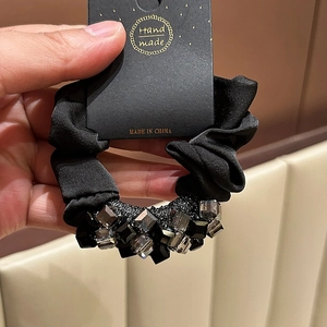 Detail of a handmade black satin scrunchie with dark grey faceted crystal beads and tag