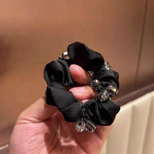 Detailed view of a black satin scrunchie featuring elegant crystal beads and a round pendant
