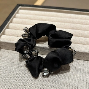Detailed close-up of elegant black satin scrunchie with sparkling grey crystal beads