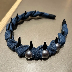 Close-up of blue denim headband with black spikes and silver pearl accents on a stand