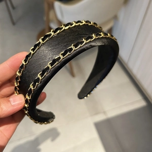 Détail d'un serre-tête large noir avec double chaîne dorée et ruban en cuir tressé