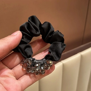 Detail of a black satin scrunchie featuring faceted gray crystal beads on soft fabric