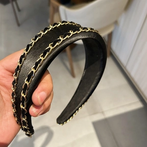 Détail d'un serre-tête en similicuir noir avec deux décorations en chaîne dorée