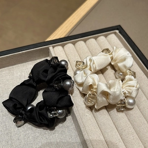 Elegant satin hair scrunchies in black and beige with pearl beads on a display tray