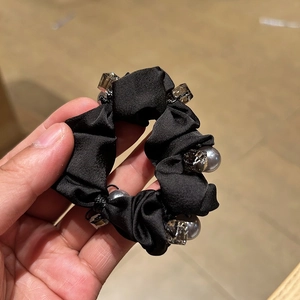 Detailed close-up of a black satin scrunchie featuring hand-sewn crystal beads and grey pearls