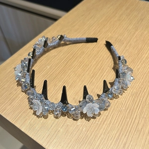 Detailed close-up of crystal lily of the valley headband with punk spikes on wood