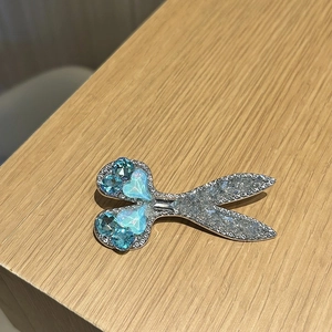 Close-up of a silver scissors-shaped hair clip with blue heart crystals and micro-pavé details
