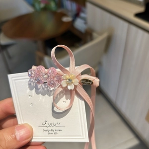 Détail de la barrette à cheveux avec nœud en ruban rose, perles de cristal et fleur blanche