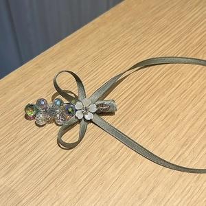 Détail de la pince à cheveux avec nœud en ruban vert olive, cristaux et petite fleur blanche