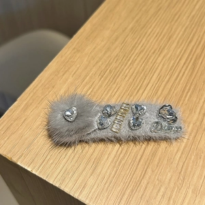 Détail d'une pince à cheveux en peluche grise avec strass et logo Dimoo en métal