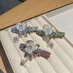 Three colorful crystal floral hair clips in blue, green and purple on a velvet display tray