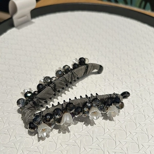 Détail d'une pince banane perlée avec perles sombres facettées et fleurs blanches