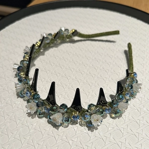 Detail of dark green fabric headband with black spikes and blue crystal flower accents