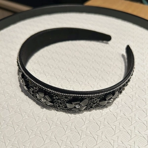 Détail d'un serre-tête baroque noir orné de cristaux et fleurs en strass sur fond blanc