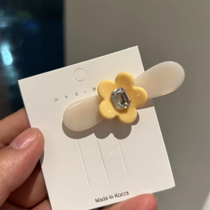 Gros plan d'une barrette à fleurs en acétate avec strass étincelant sur carte blanche