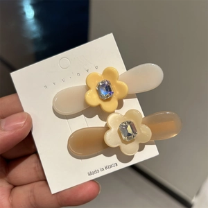 Gros plan de deux pinces à cheveux fleur en acétate avec strass rectangulaires sur carte