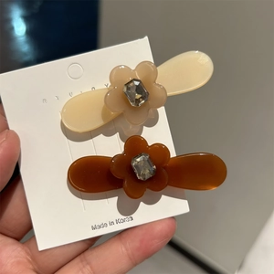 Détail de petites barrettes fleurs en acétate avec strass en beige et ambre