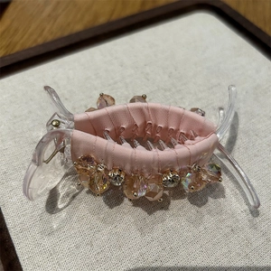 Close-up of pink silk fabric hair claw clip with colorful crystal beads on beige texture