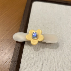 Détail d'une pince à cheveux en acétate avec fleur jaune et strass carré brillant