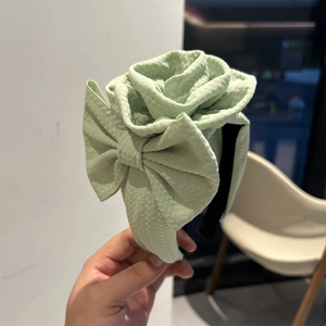 Detail of light green fabric headband with large 3D rose and bow in soft texture