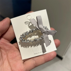 Détail de la pince à cheveux avec perles argentées et nœud gris sur une carte