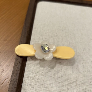 Détail d'une petite pince à cheveux fleur en acétate avec un strass central brillant