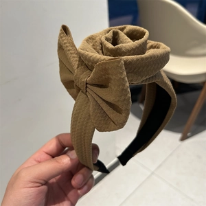 Detail view of brown fabric headband with 3D rose flower and bow texture close-up