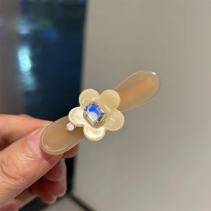 Détail macro d'une barrette en acétate ambré avec décor floral en strass en main