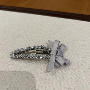 Détail d'une barrette BB perlée argentée avec un nœud en ruban gris sur tissu