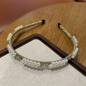 Detail of gold woven headband with white pearls and rhinestones on wood texture