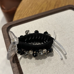 Detail of elegant black fabric hair claw clip with faceted dark crystals on linen tray