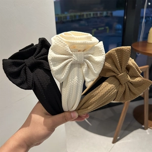 Detailed close-up of textured oversized bow headbands in black, beige, and khaki colors