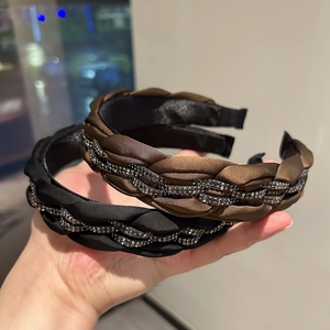 Detail handgehaltener geflochtener Satin-Haarreifen in Schwarz und Kaffee mit Strass