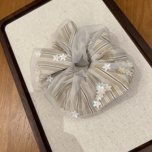 Detail of floral sequin tulle scrunchie on linen board with warm lighting