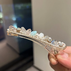 Macro shot of handmade hair clip featuring crystals, pearls, and blue gemstone details