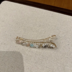Detailed view of handmade duckbill hair clip with amber base, pearls, and blue crystals