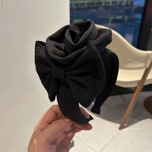 Detailed close-up of a black textured floral headband with ornate 3D rose decoration