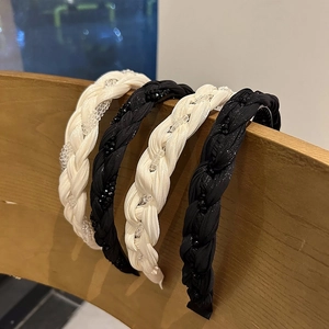 Close-up of braided crystal headbands in black and cream silk on a wooden stand