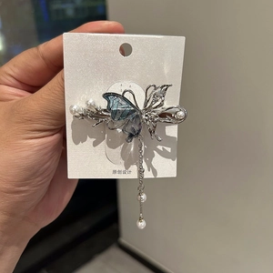 Dettaglio di un fermaglio a farfalla in argento con ali blu e nappe di perle eleganti