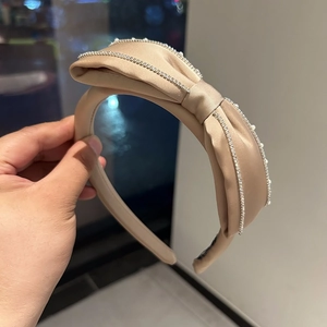 Detail of beige satin headband featuring a large bow and rhinestone edges