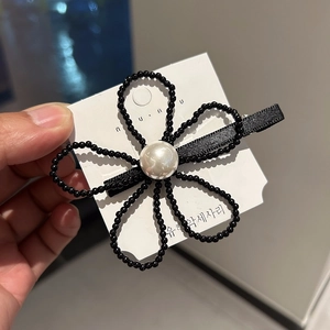 Macro d'une pince à cheveux fleurie en perles noires avec une grande perle blanche centrale